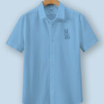 Light blue oversized cotton shirt with detailed vulpine (fox) embroidery on the chest, displayed on a wooden hanger.