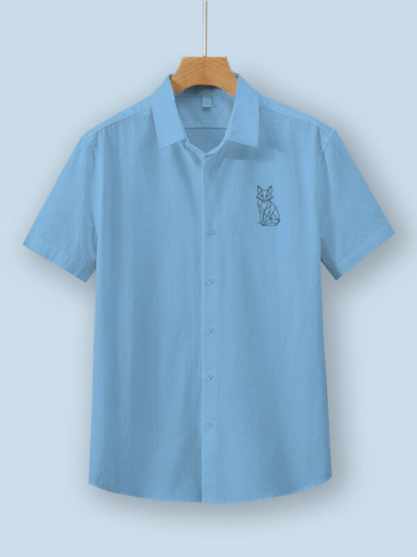 Light blue oversized cotton shirt with detailed vulpine (fox) embroidery on the chest, displayed on a wooden hanger.
