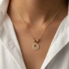 A gold circular halo pendant necklace with crystal accents, symbolizing radiance and renewal, styled with a white shirt