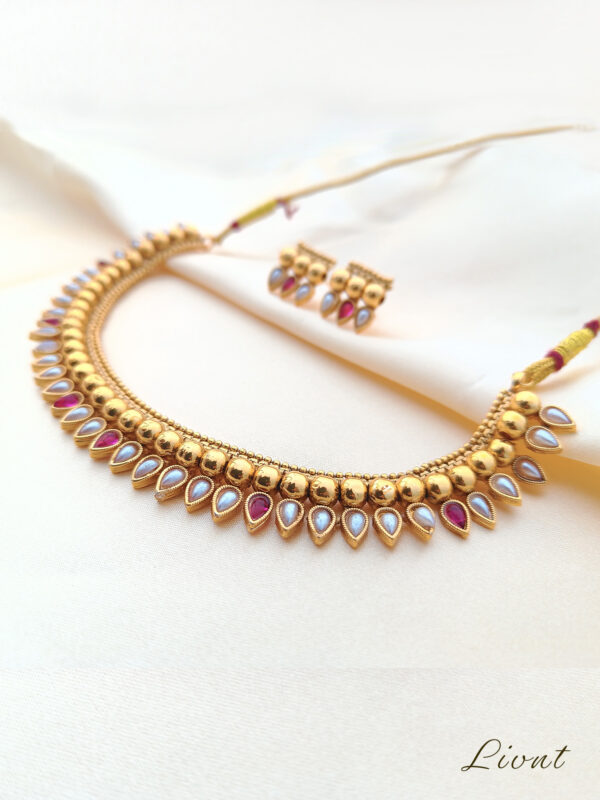 Close-up of LIVNT Ruby & Pearl Heritage Necklace showing intricate beaded chain, pearl and ruby teardrop settings, and hypoallergenic stainless steel construction with gold finish