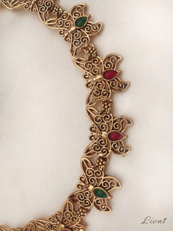 Close-up detail of the Butterfly Gem Set necklace, showing intricate filigree work and red and green stones.