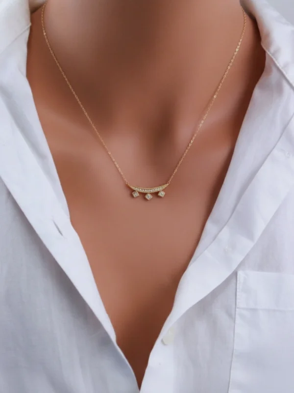 A gold crescent necklace with three square-cut crystal drops, worn with a white shirt, symbolizing elegance and modern geometry.