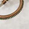 Traditional Kerala gold necklace set with green emerald palakka mango leaf design and matching earrings on cream fabric