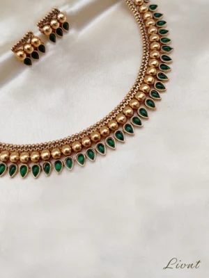 Traditional Kerala gold necklace set with green emerald palakka mango leaf design and matching earrings on cream fabric
