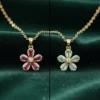 A side-by-side comparison of the LIVNT Scarlet Flower necklace in two colors: ruby-red and ocean-green. Each gold pendant features five baguette-cut gemstone petals with a central diamond, set against a dark greA side-by-side comparison of the LIVNT Scarlet Flower necklace in two colors: ruby-red and ocean-green. Each gold pendant features five baguette-cut gemstone petals with a central diamond, set against a dark green silk backdrop.en silk backdrop.