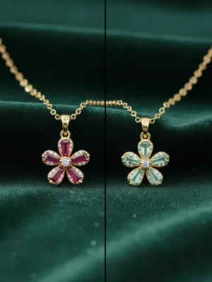 A side-by-side comparison of the LIVNT Scarlet Flower necklace in two colors: ruby-red and ocean-green. Each gold pendant features five baguette-cut gemstone petals with a central diamond, set against a dark greA side-by-side comparison of the LIVNT Scarlet Flower necklace in two colors: ruby-red and ocean-green. Each gold pendant features five baguette-cut gemstone petals with a central diamond, set against a dark green silk backdrop.en silk backdrop.