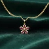 A gold Scarlet Flower pendant necklace with five ruby-red baguette-cut gemstone petals and a central diamond, resting on a dark green silk background.