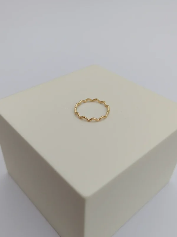 A delicate gold Wave Ring with a continuous ripple design, professionally photographed on a minimalist white display block against a clean white background.