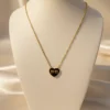 A gold 11:11 Heart Anti-Tarnish Necklace, featuring a heart pendant with '11:11' in black enamel inscription, displayed on an off-white jewelry bust. A draped cream silk background is visible behind.
