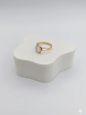 Angled side view of the elegant Moonlit Ring, showing the texture of the gold band and the shimmer of the central white pearl stone on a white display block.