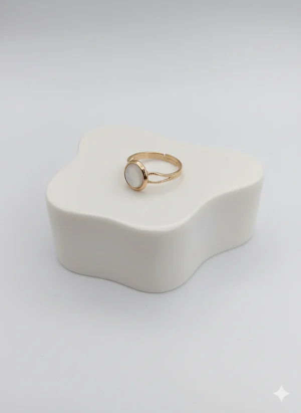 Angled side view of the elegant Moonlit Ring, showing the texture of the gold band and the shimmer of the central white pearl stone on a white display block.