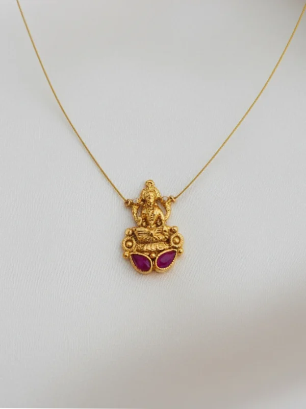 Front view of a traditional South Indian Goddess Lakshmi locket crafted in matte gold, featuring two oval ruby-toned Kemp stones, hung on a barely visible gold micro-chain against a clean white backdrop.