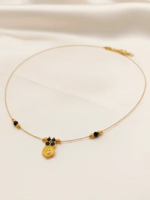 The Mangal Invisible Chain necklace with black beads and a gold kasu coin pendant resting on a white silk background.