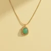 A high-quality product shot of a gold pendant necklace on a solid cream-colored background. The necklace features a smooth snake chain and a cushion-cut, light green stone in a gold setting with a twisted rope border, with a soft shadow to the side.
