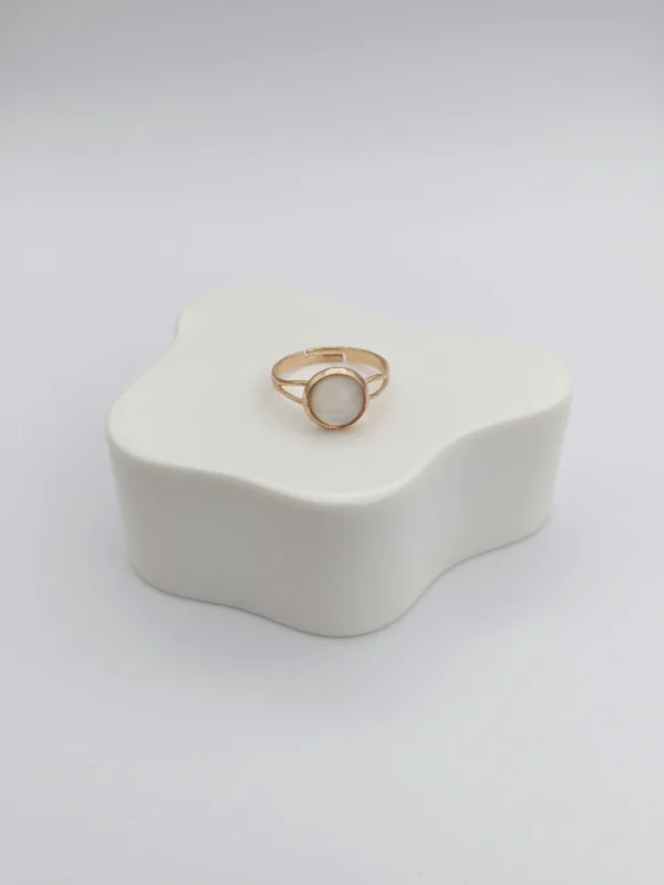 A lifestyle shot of the Moonlit Ring from the side, showing its delicate profile and adjustable gold-tone band on a clean white surface.