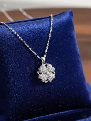 Spinning Heart Clover necklace on royal blue velvet jewelry pillow, close-up, silver pave heart pendant.