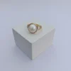 The Orb Ring shown from the front, featuring a large white pearl set in a minimalist gold band, resting on a clean white block.Centered in elegance. The Orb Ring.