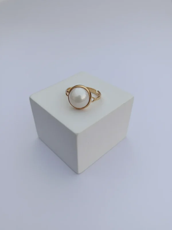 The Orb Ring shown from the front, featuring a large white pearl set in a minimalist gold band, resting on a clean white block.Centered in elegance. The Orb Ring.