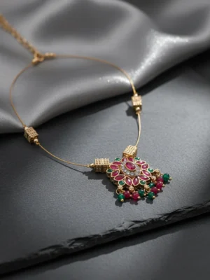 Luxury handcrafted Petal Drop Invisible Necklace with ruby, emerald, and gold-plated floral pendant resting on a soft grey silk background — symbolic jewelry by LIVNT representing grace and renewal.