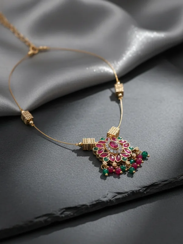 Luxury handcrafted Petal Drop Invisible Necklace with ruby, emerald, and gold-plated floral pendant resting on a soft grey silk background — symbolic jewelry by LIVNT representing grace and renewal.