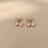 A pair of Cupid's Bow Earrings in rose gold with opalescent heart charms, styled on a neutral beige background with soft, elegant lighting.