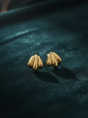 Golden shell stud earrings elegantly placed on a luxurious dark teal velvet fabric.