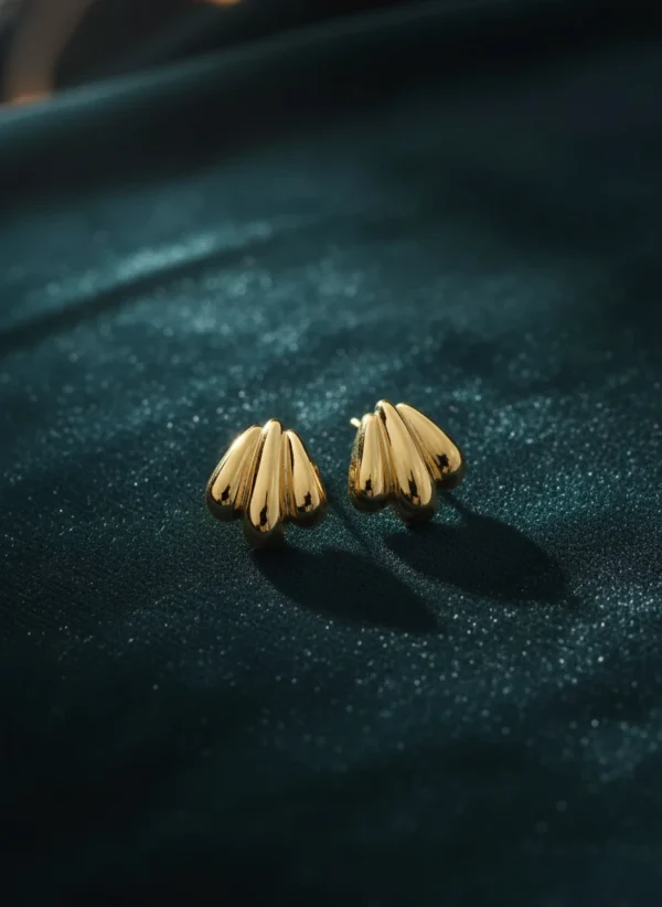 Golden shell stud earrings elegantly placed on a luxurious dark teal velvet fabric.