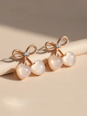 An angled, professional shot of the rose gold Cupid's Bow Earrings, showing their slight dimension and the pearlescent sheen of the heart stones.