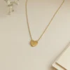 A gold 11:11 Heart Anti-Tarnish Necklace displayed on a plain white surface, alongside delicate white baby's breath flowers and a stack of cream-colored stationery cards. The heart pendant is prominently centered.