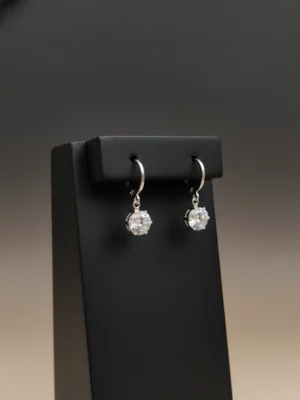 Pair of silver huggie hoop earrings with heart-shaped cubic zirconia drops displayed on a product card.