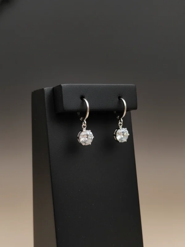 Pair of silver huggie hoop earrings with heart-shaped cubic zirconia drops displayed on a product card.