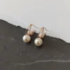 Close-up of two Lumina Modern Pearl Stud earrings on a torn white paper and dark marble background, showcasing the design.