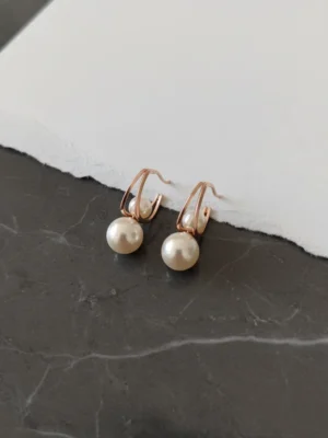 Close-up of two Lumina Modern Pearl Stud earrings on a torn white paper and dark marble background, showcasing the design.