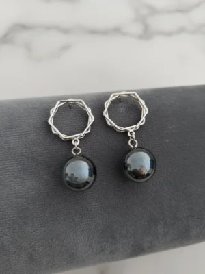 A pair of LIVNT Onyx Octagon Drop Earrings on a dark grey velvet display, featuring sterling silver geometric octagonal tops and smooth, round polished black onyx drops. The background is a soft, blurred white marble texture.