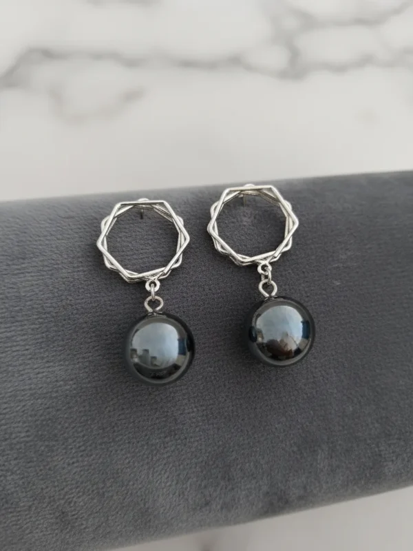 A pair of LIVNT Onyx Octagon Drop Earrings on a dark grey velvet display, featuring sterling silver geometric octagonal tops and smooth, round polished black onyx drops. The background is a soft, blurred white marble texture.