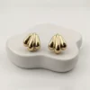 Pair of golden shell-inspired stud earrings on a minimalist white organic-shaped block.