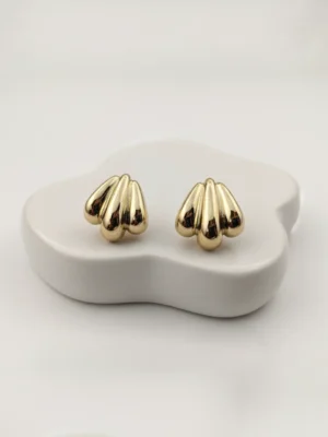 Pair of golden shell-inspired stud earrings on a minimalist white organic-shaped block.