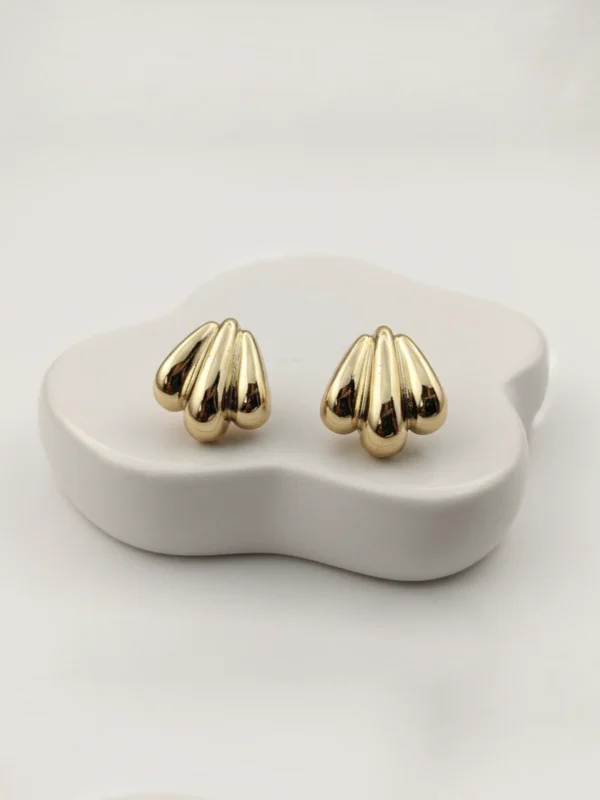 Pair of golden shell-inspired stud earrings on a minimalist white organic-shaped block.