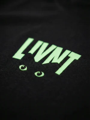 Close-up of LIVNT glow-in-the-dark cat eye logo on black t-shirt